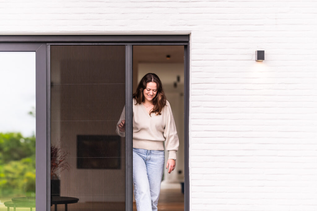 Vrouw die door een plissé hordeur stapt